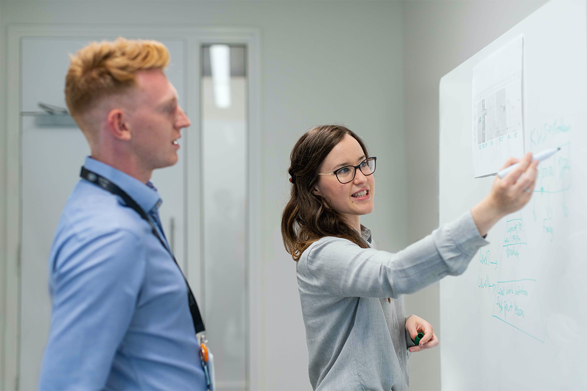 Female showing male coworker a problem on a whiteboard